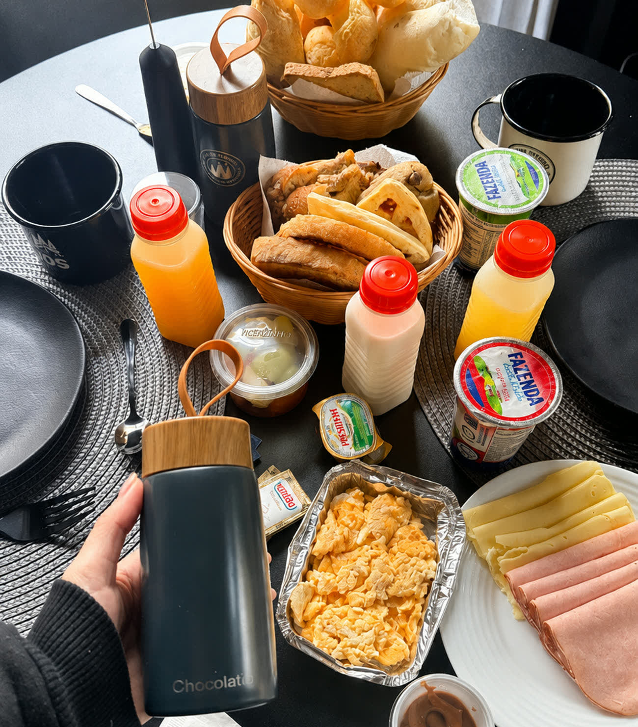 A cesta de café da manhã servida na mesa da cabana, com pães, ovos, frios, frutas e sucos